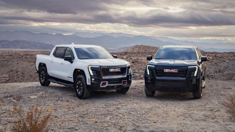 Two GMC Sierra EV electric pickup trucks in a desert landscape